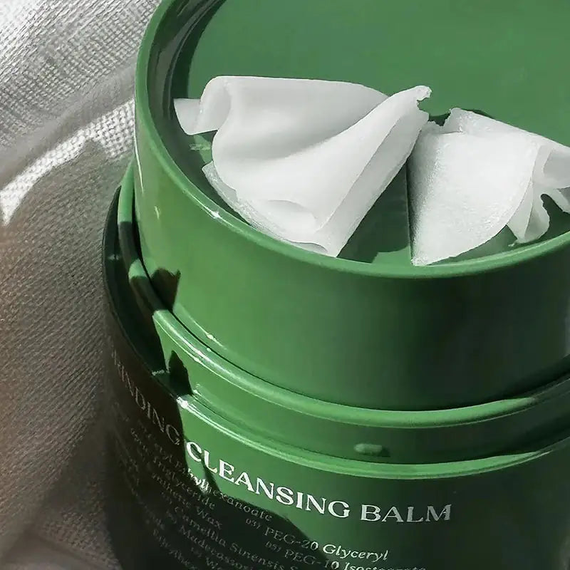 Open groene cleansing balm-pot met witte cosmetische vlokken.