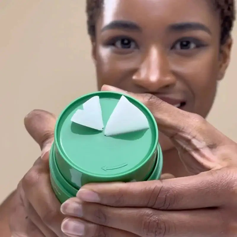Groene cleansing balm in pot vastgehouden met open deksel en witte stroken.