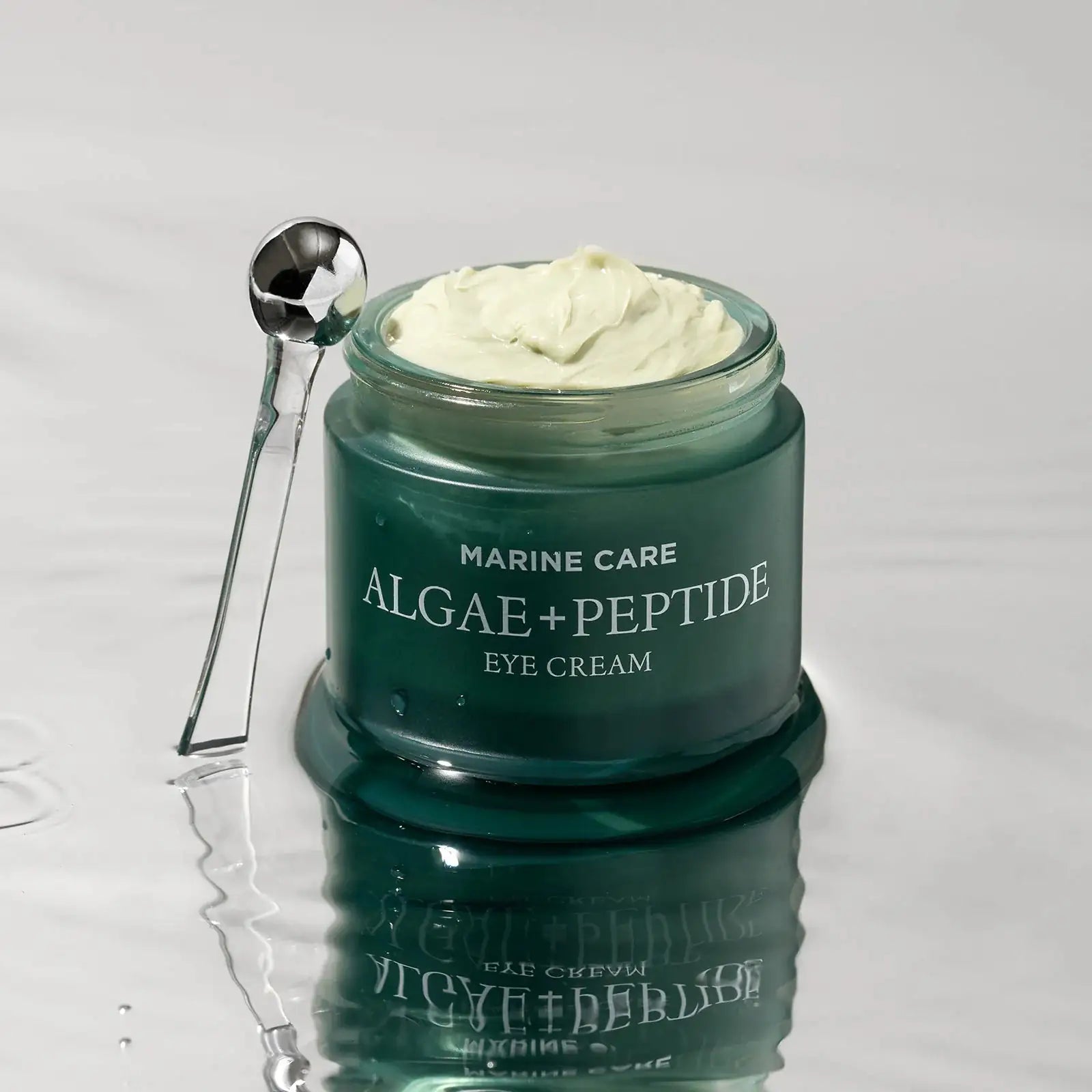 Oogcrème in groen glazen potje met witte crème en metalen applicatorlepel