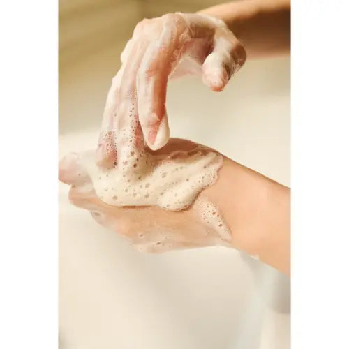 Handen die een rijk schuimende gezichtsreiniger aanbrengen tijdens het wassen van het gezicht.