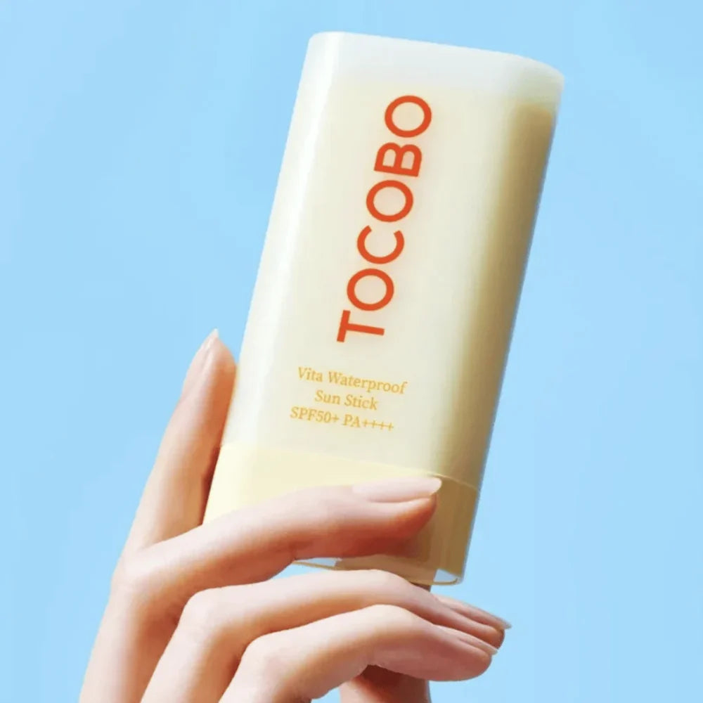 TOCOBO Vita Waterproof Sun Stick gehouden door hand tegen blauwe lucht