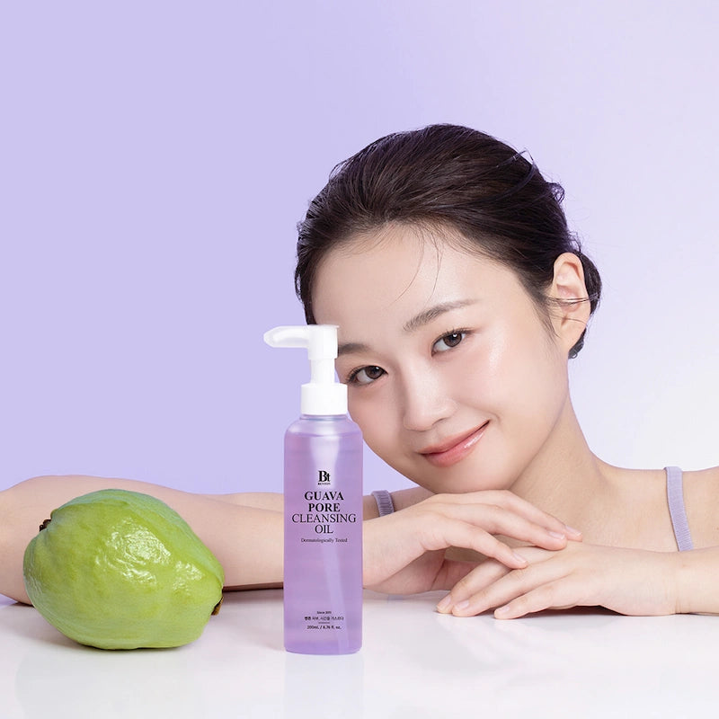 Model met guava: Model met stralende huid naast de Benton Guava Pore Cleansing Oil 200ml en een verse guava op lichtpaarse achtergrond