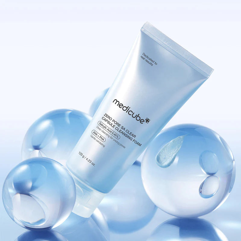 Lifestyle — Medicube Zero Pore SA Clear Capsule Cleansing Foam 120g tube naast blauwe glazen bollen op lichtblauwe achtergrond.