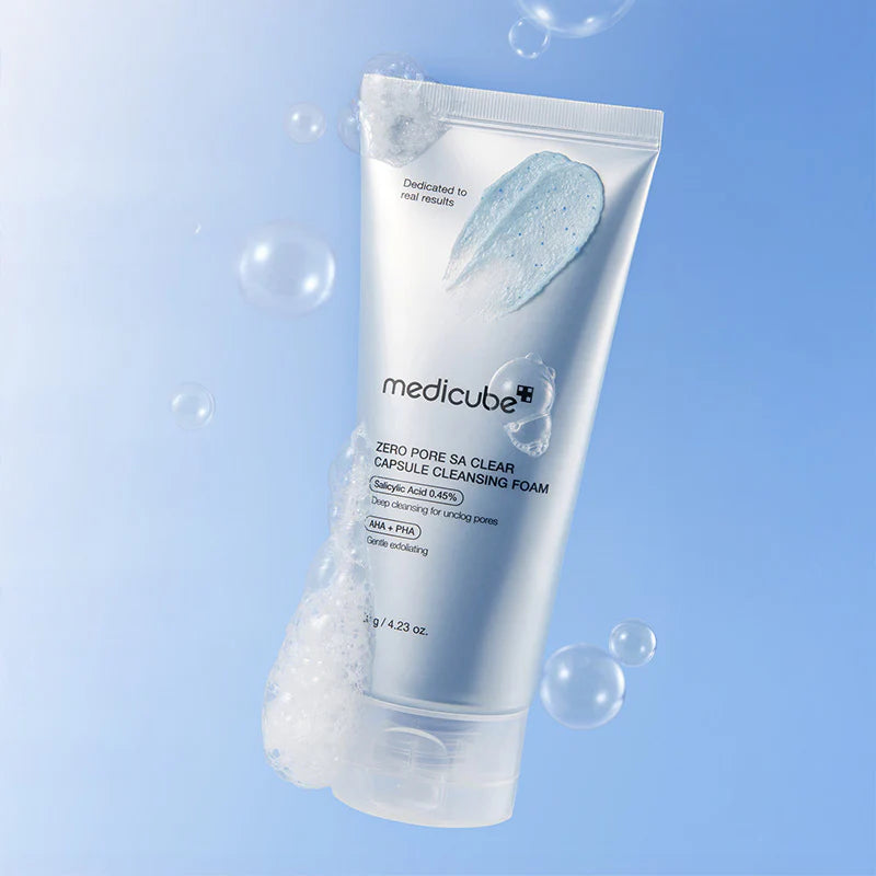 Medicube Zero Pore SA Clear Capsule Cleansing Foam tube zwevend tegen blauwe lucht achtergrond met zeepbellen en blauwe schuimtextuur.