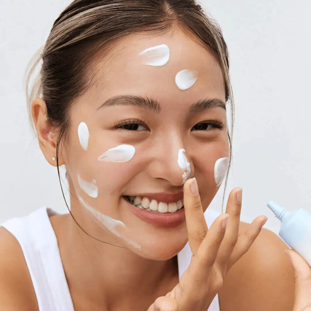 Zonnebrandcrème tube bij gezicht, meerdere witte crème stippen op huid.