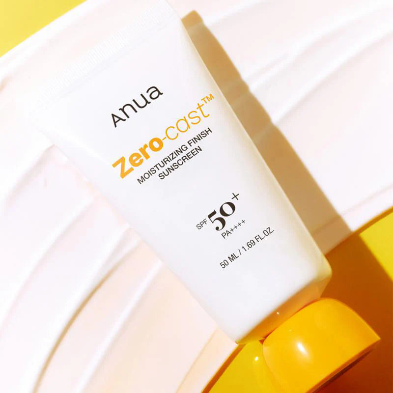 Anua Zero-Cast Moisturizing Finish Sunscreen SPF 50 tube liggend op witte crèmetextuur met gele achtergrond