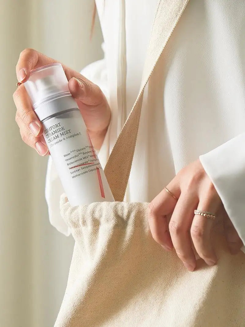 Ceramide crème-mistfles met pompje in hand, naast beige kleding