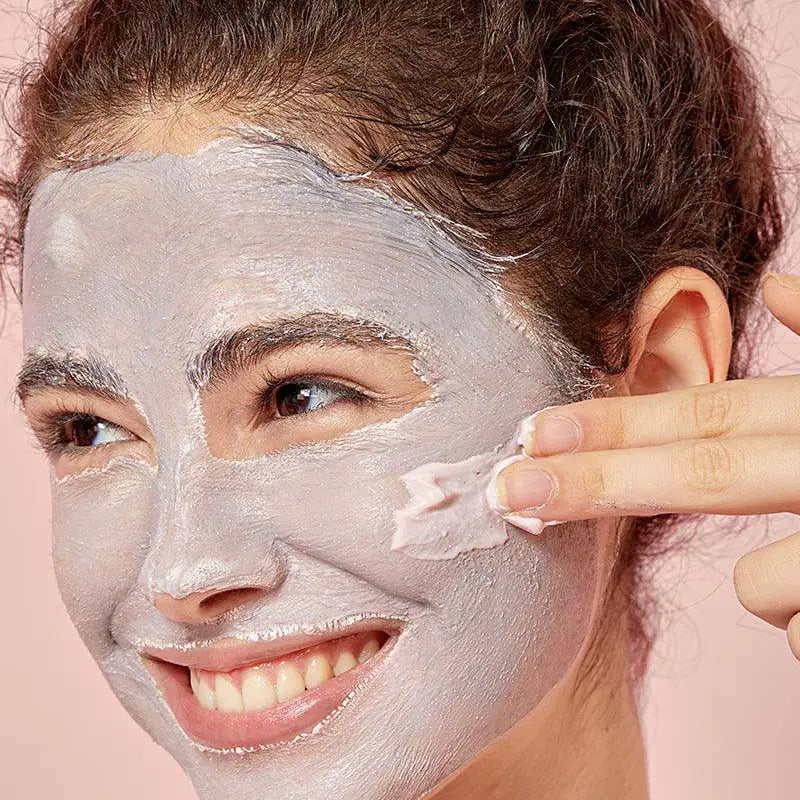 Vrouw met gezichtsmasker; hand brengt witte maskerlaag aan langs wang en kaak
