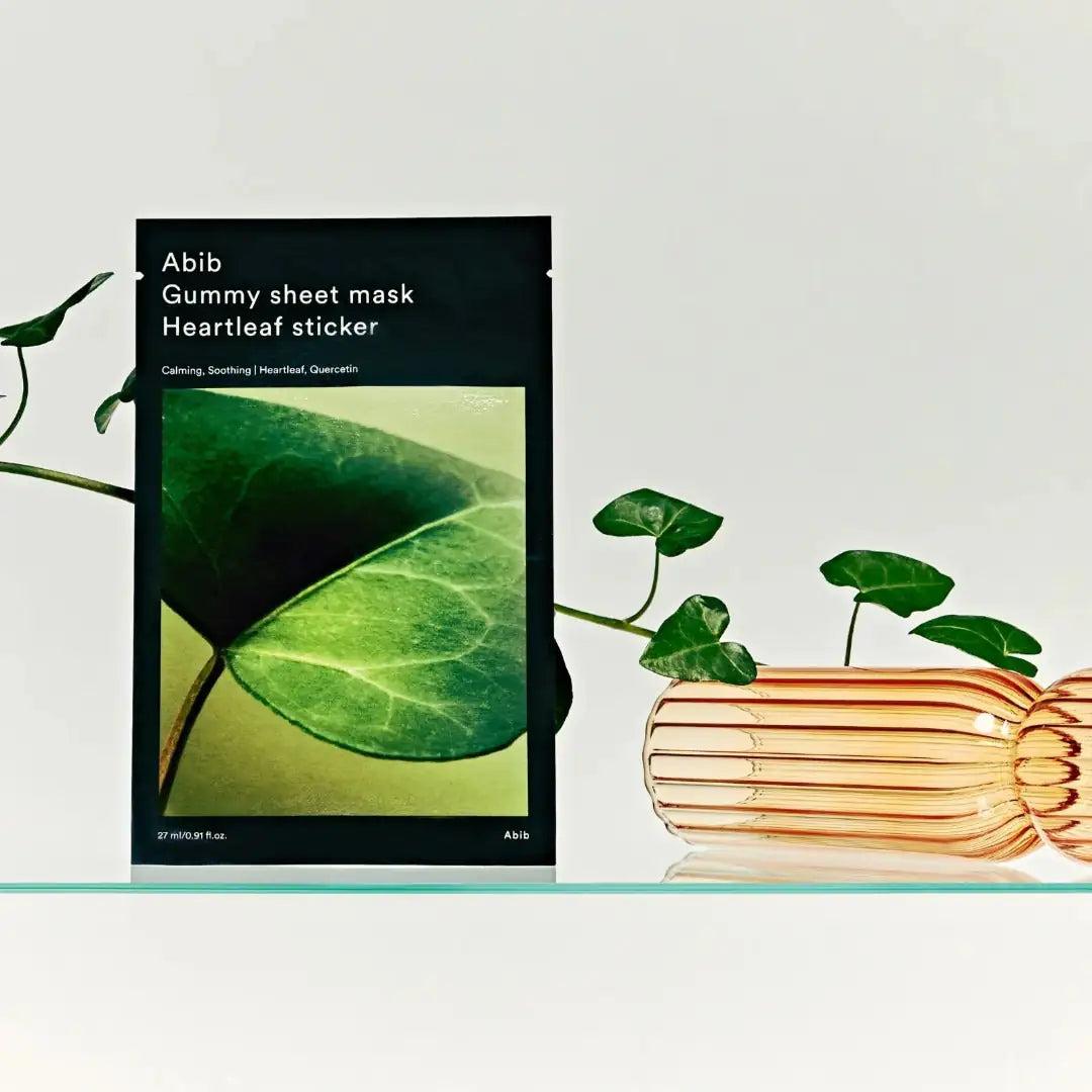 Abib Gummy Sheet Mask Heartleaf Sticker Sheetmasker verpakking met groene leaf-print naast opgerolde maskerstrookjes