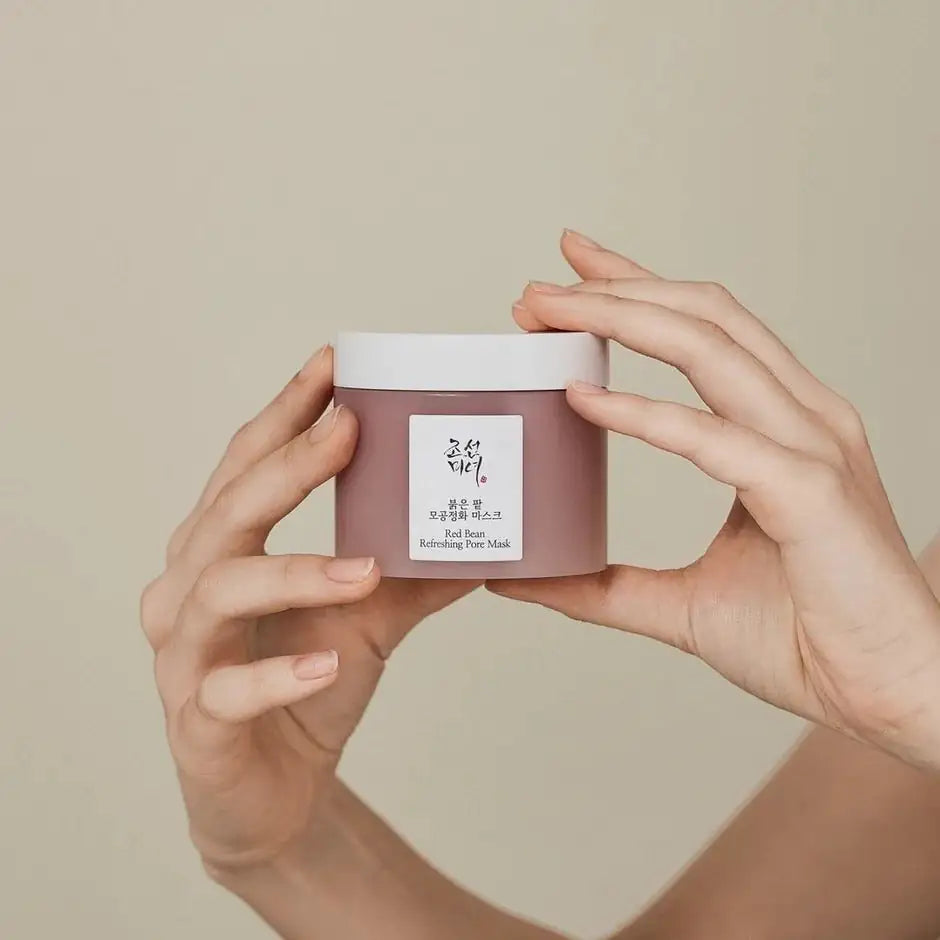 Ronde pot met wit deksel en etiket van rodebonen poriënmasker, vastgehouden door handen