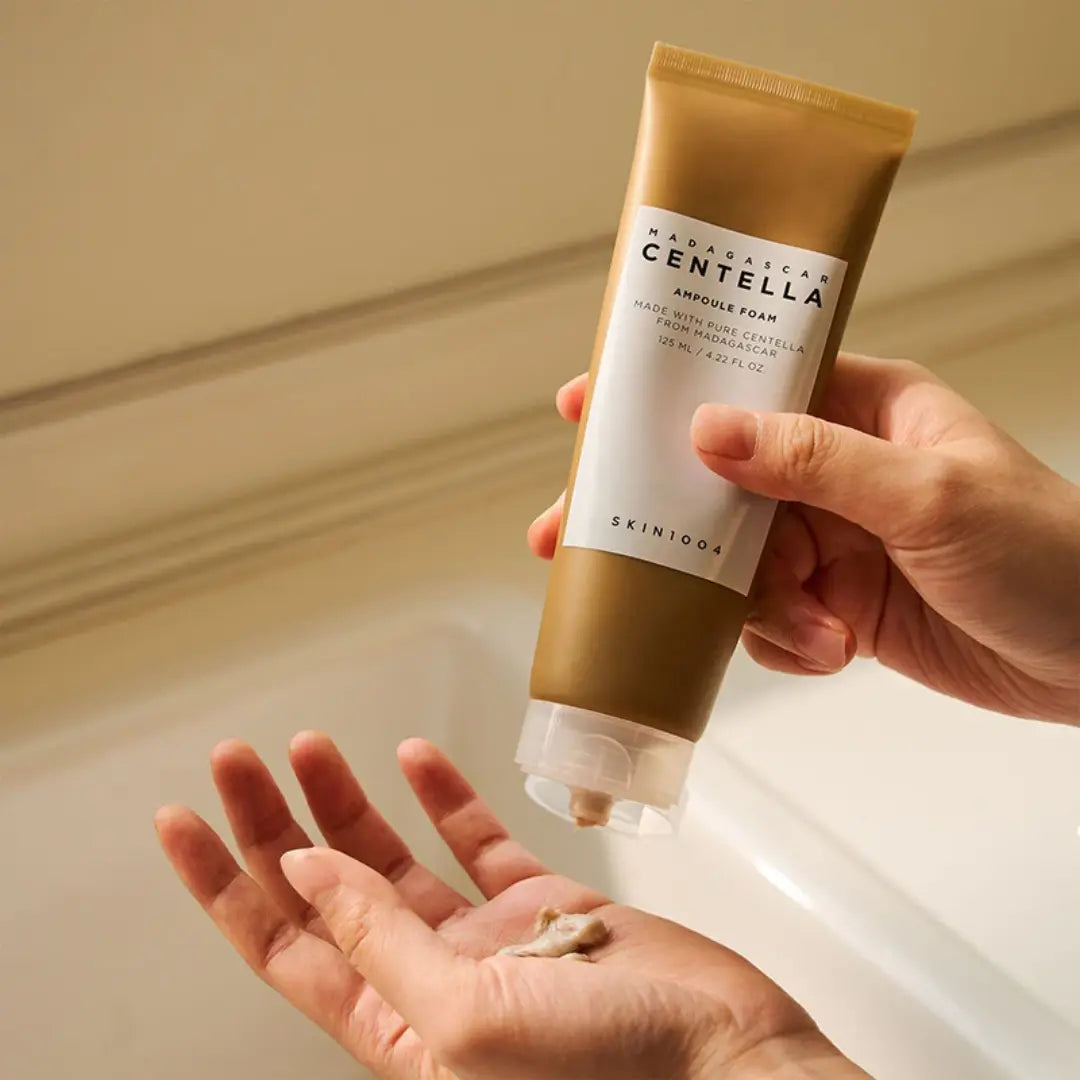 Iemand die SKIN1004 Madagascar Centella Ampoule Foam uit de tube op de hand aanbrengt bij de wastafel.