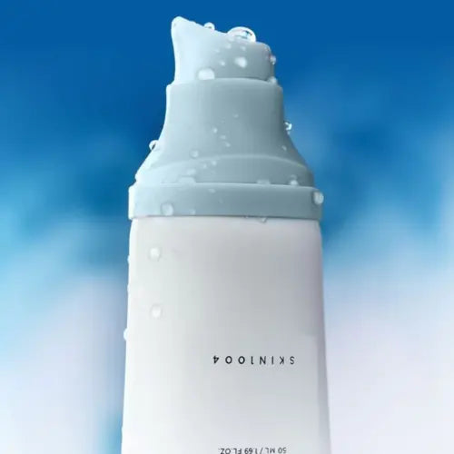 Close-up van de pompflacon van SKIN1004 Hyalu-Cica Water-Fit Sun Serum met waterdruppels op de dop tegen een blauwe achtergrond